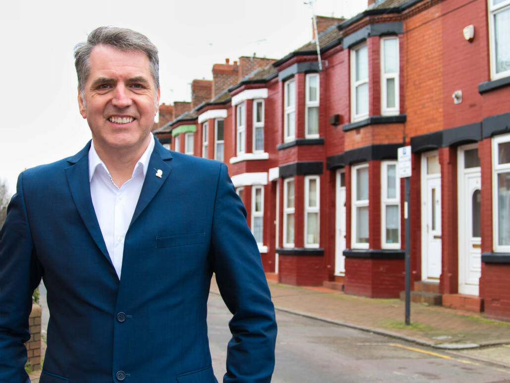 Mayor Steve Rotheram standing on a street in front of a row of terraced houses