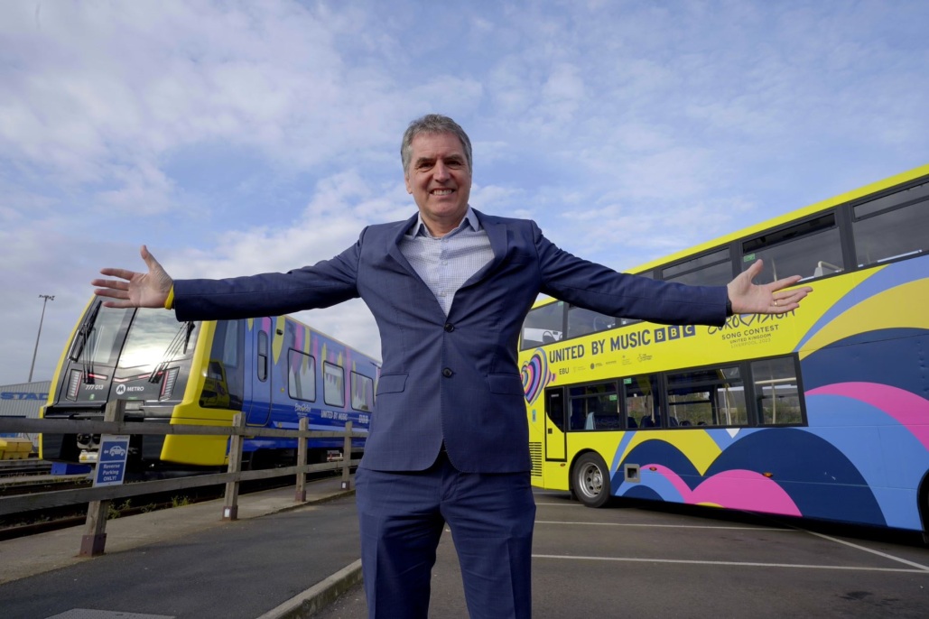 Mayor Steve Rotheram arms wide in front of a bus and a train
