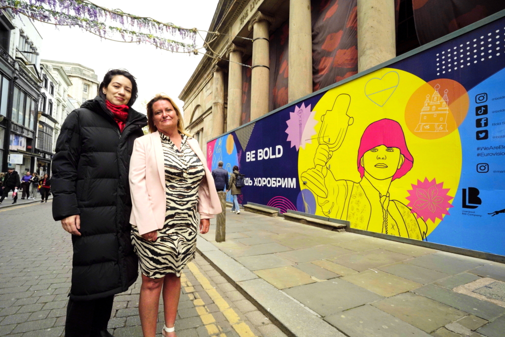 Two women stand in front of a billboard in Liverpool's Bold Street