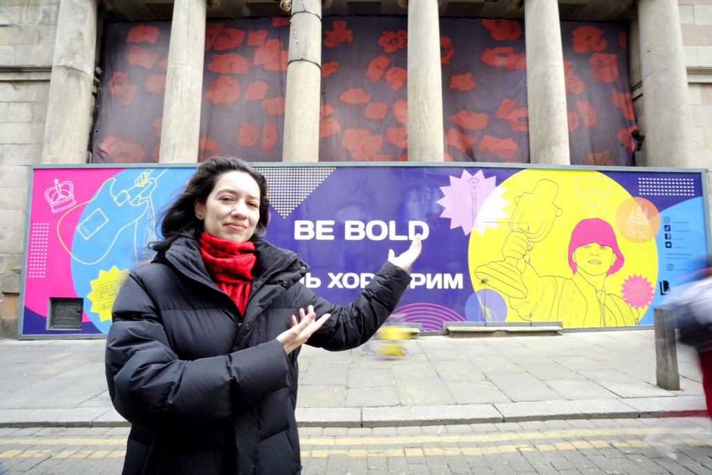Woman stands in front of a Eurovision-themed artwork on a large street-level billboard