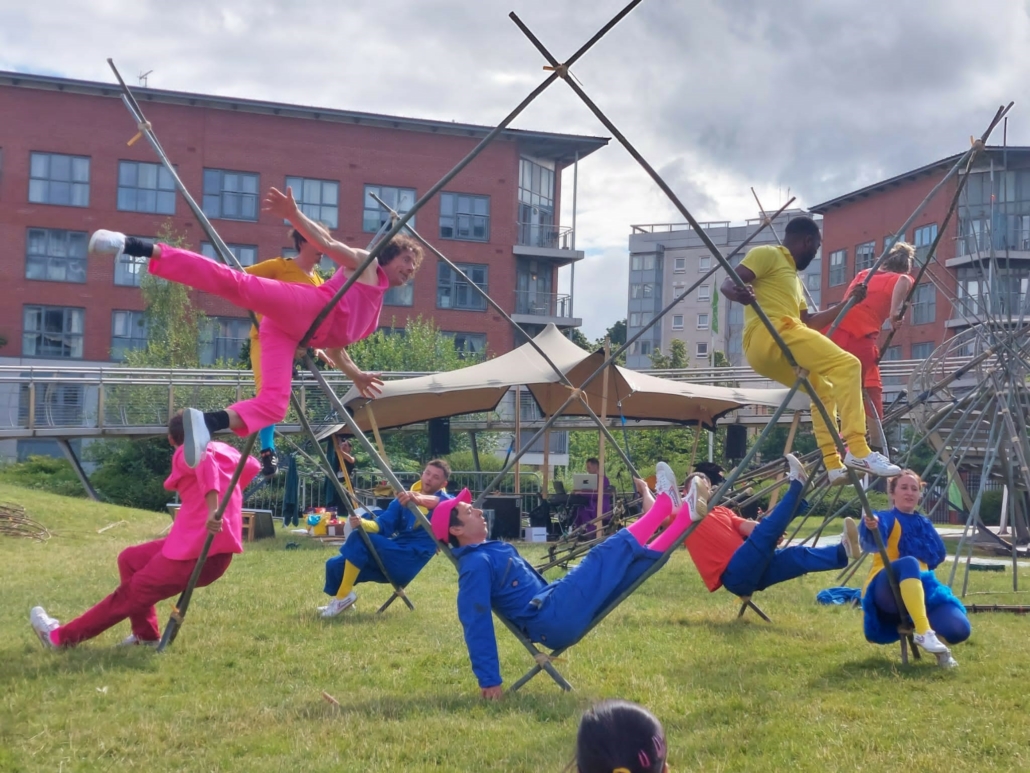 People wearing different bright colours all balance on a large bamboo structure.
