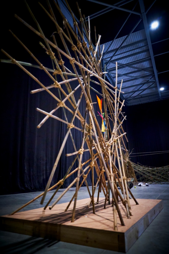 A bamboo sculpture creating a frame which you could stand behind and take a photo of yourself in the middle it's made of lots of straight pieces of bamboo criss crossed creating a star like shape.