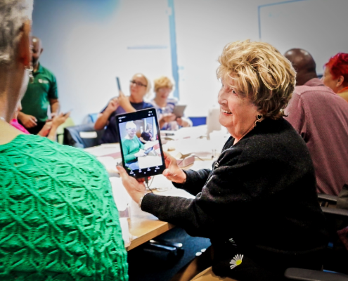 A woman holding a digital tablet and tilting it to show the person next to her. She's smiling.