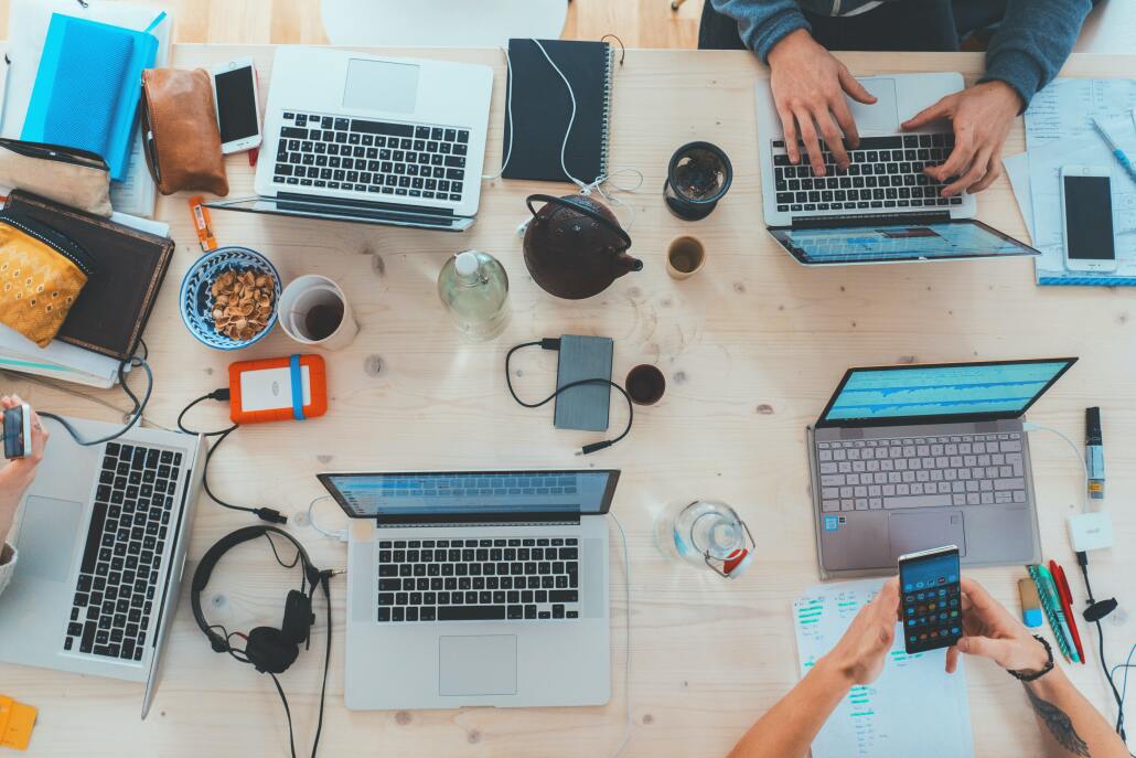 A bird's-eye view of the table. On the table are 5 laptops arranged in a circle, there's also a number of tablets and phones scattered on the table.