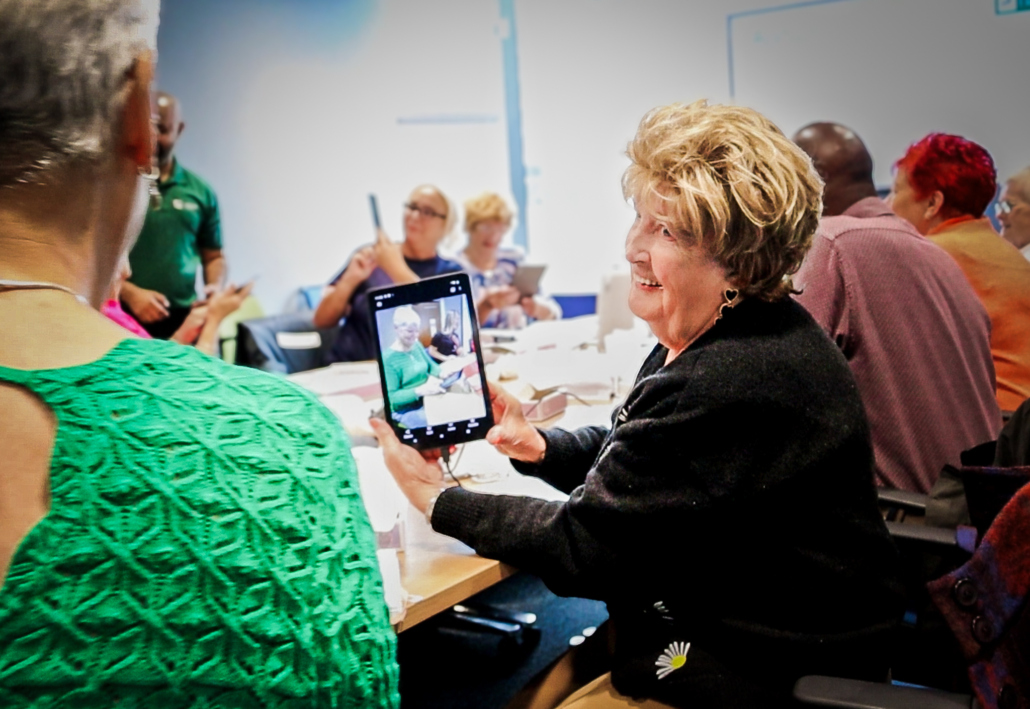 A woman holding a digital tablet and tilting it to show the person next to her. She's smiling.