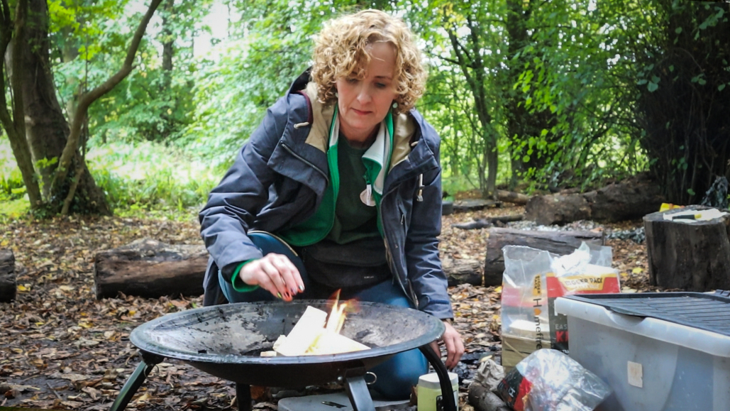 A woman makes a fire as part of a forest skills course
