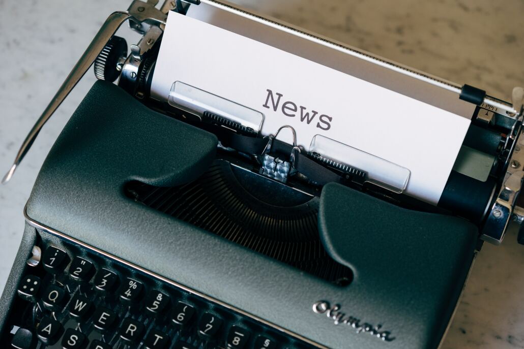 A typewriter with a piece of paper coming out of it. The piece of paper has 'news' typed on it.