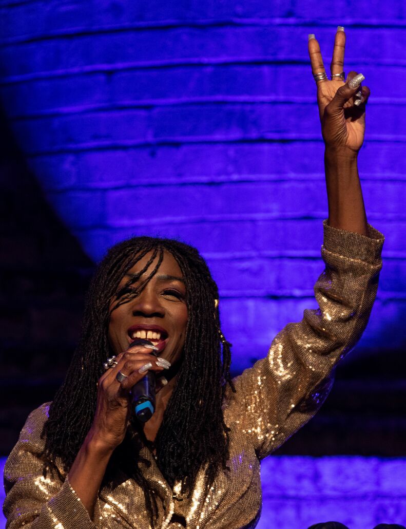 Heather Small holding a microphone and raising her hand waving to the crowd