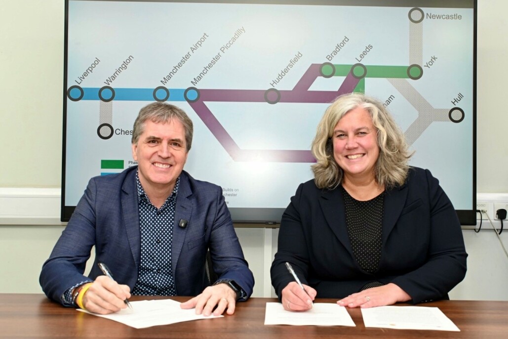 Mayor Steve Rotheram and Heidi Alexander MP sat at a table signing a compact agreement for Northern Powerhouse Rail, with a display behind them showing the map of the proposed new line.