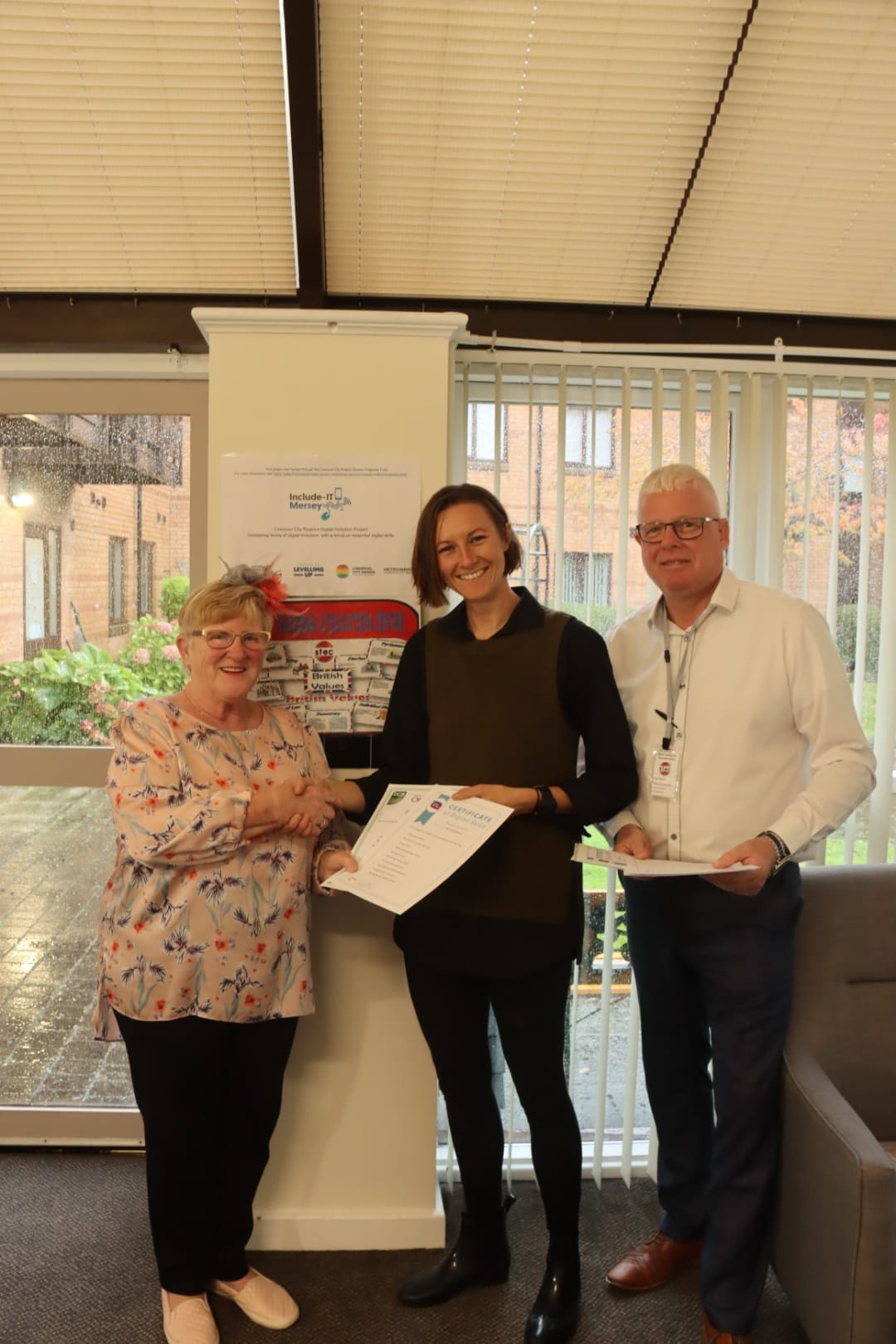 A woman being presented a certificate by two people. She's shaking hands with one of them.