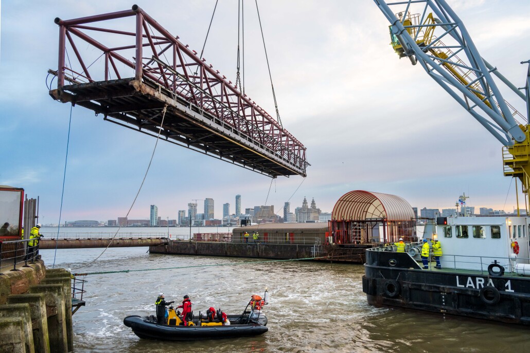 The linkspan bridge being hoisted by a crane mid air over the Mersey