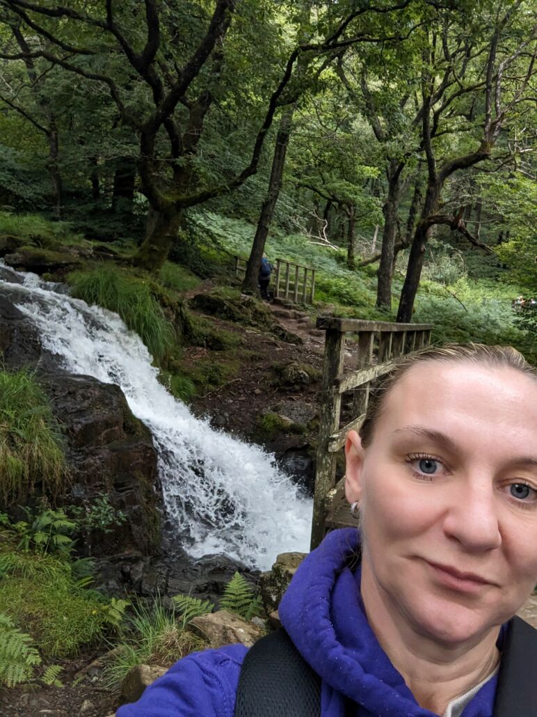 Housing First support worker standing in a forest with a river behind her